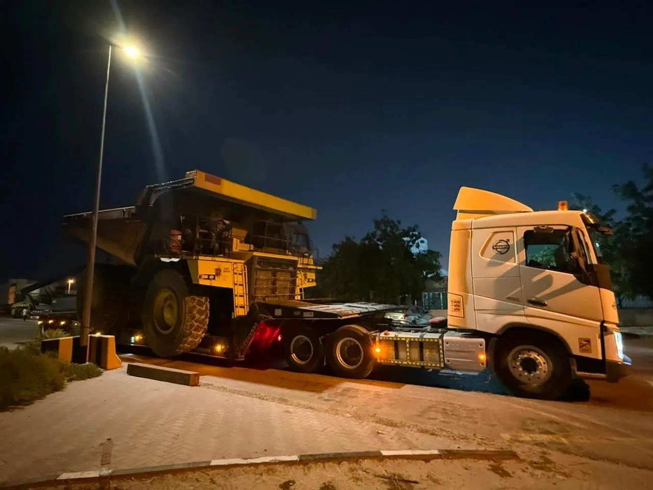 Volvo FH prime mover with a rigid dump truck loaded on a lowbed trailer at night