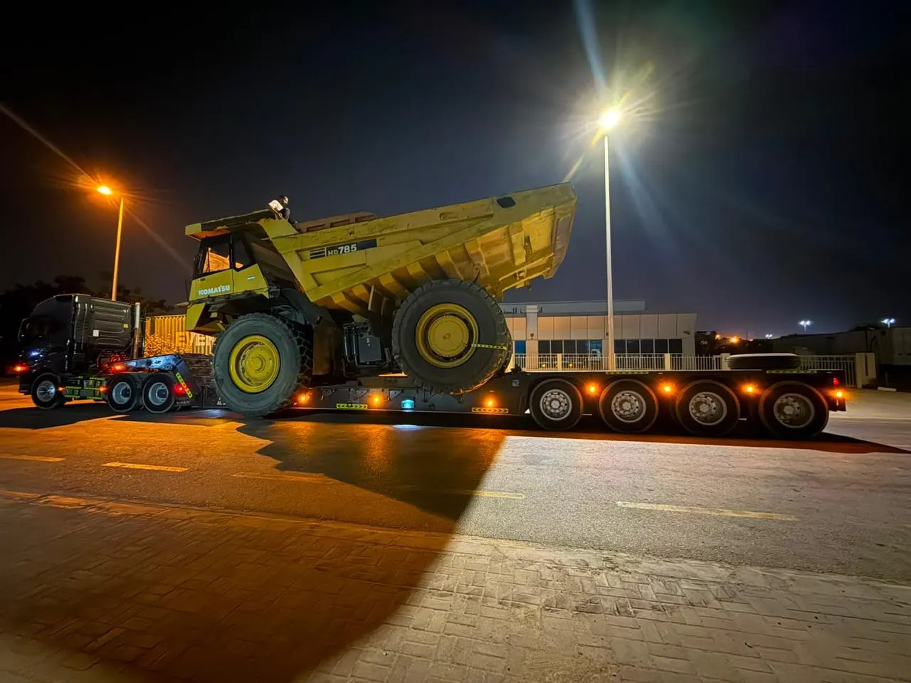 Komatsu HD785 rigid dump truck loaded on a 4-axle lowbed trailer under floodlights at night