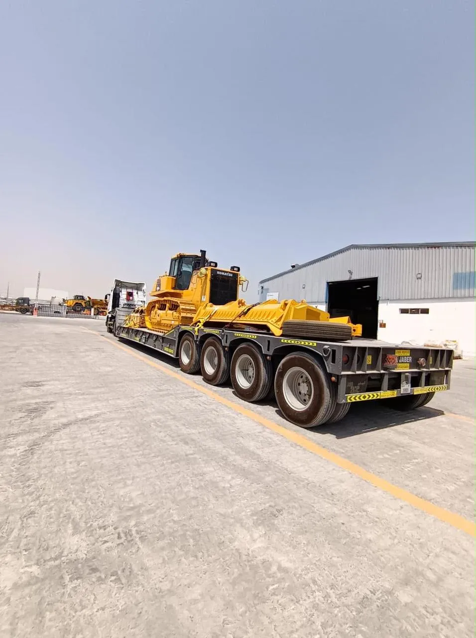 Komatsu tracked bulldozer loaded on an Al Jaber low-bed trailer in the yard
