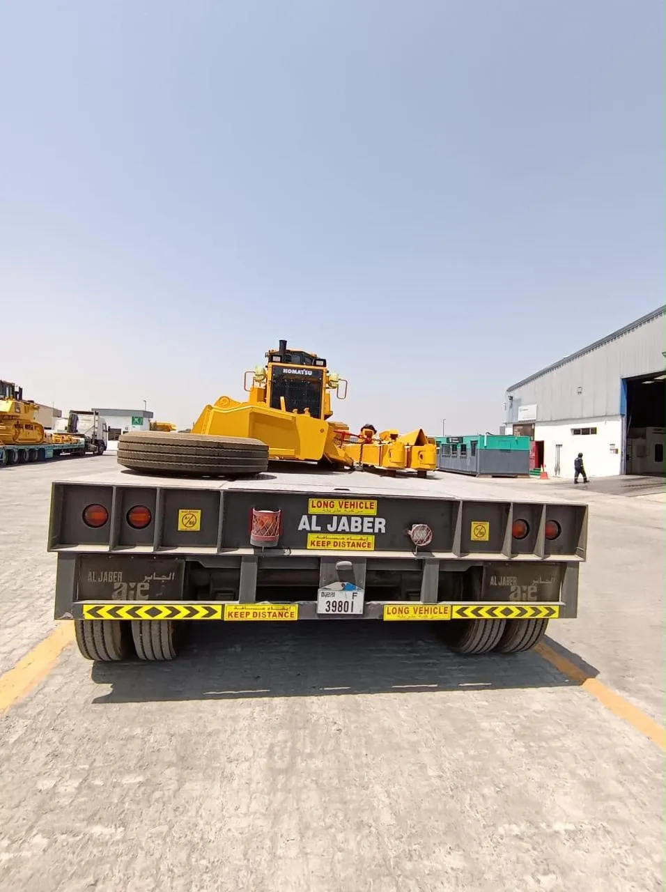 Komatsu wheel loader staged behind an Al Jaber low-bed trailer at the equipment yard