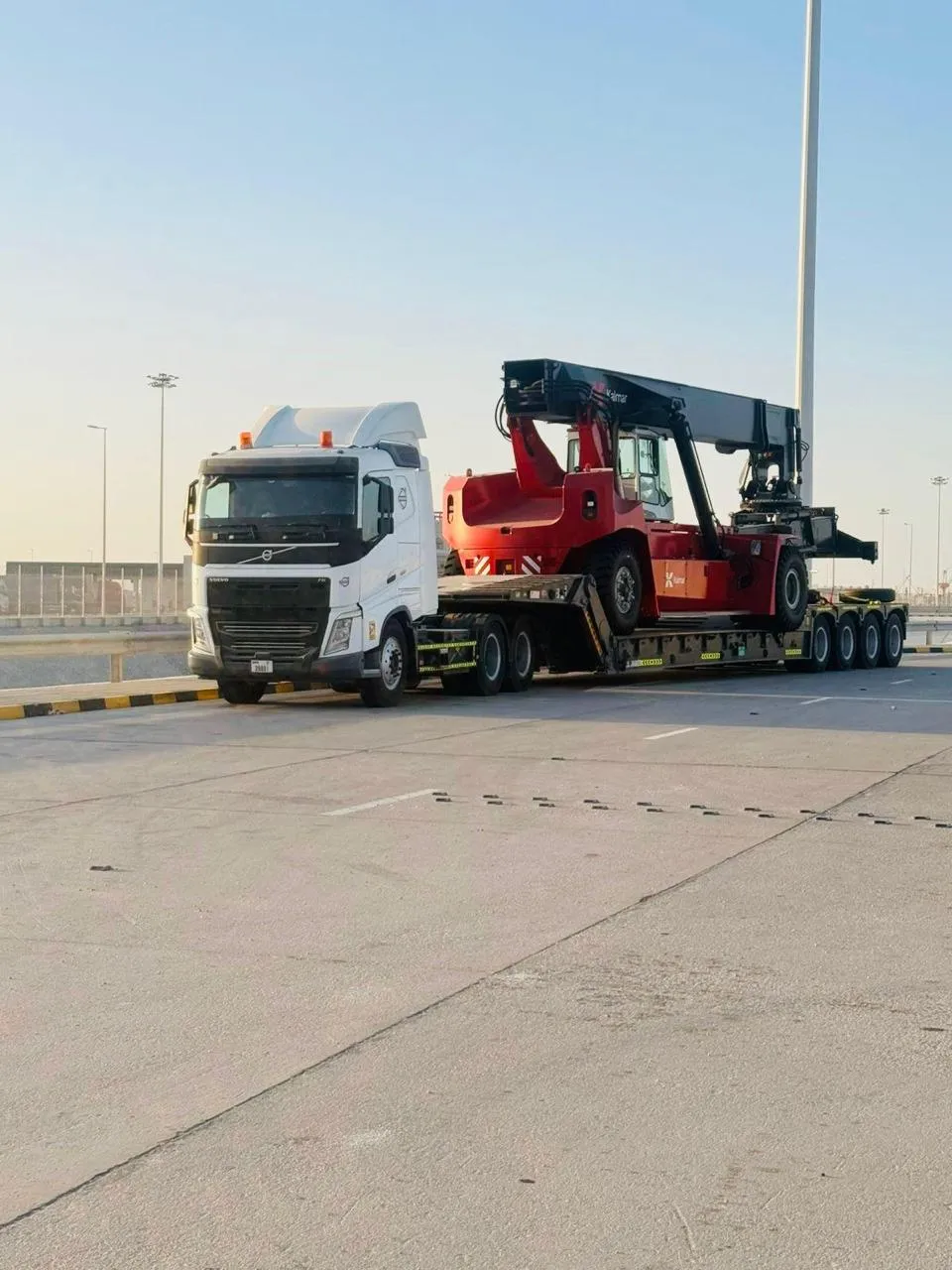 Red Kalmar reach stacker loaded on a multi-axle low-bed trailer near a UAE port